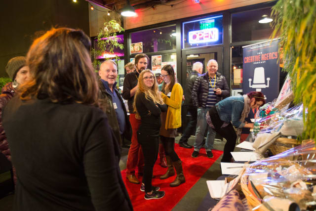 Guests mingling at the Love Bomb 2017 event, featuring a red carpet entrance, vibrant atmosphere, and a display of auction items supporting My Voice Music nonprofit.